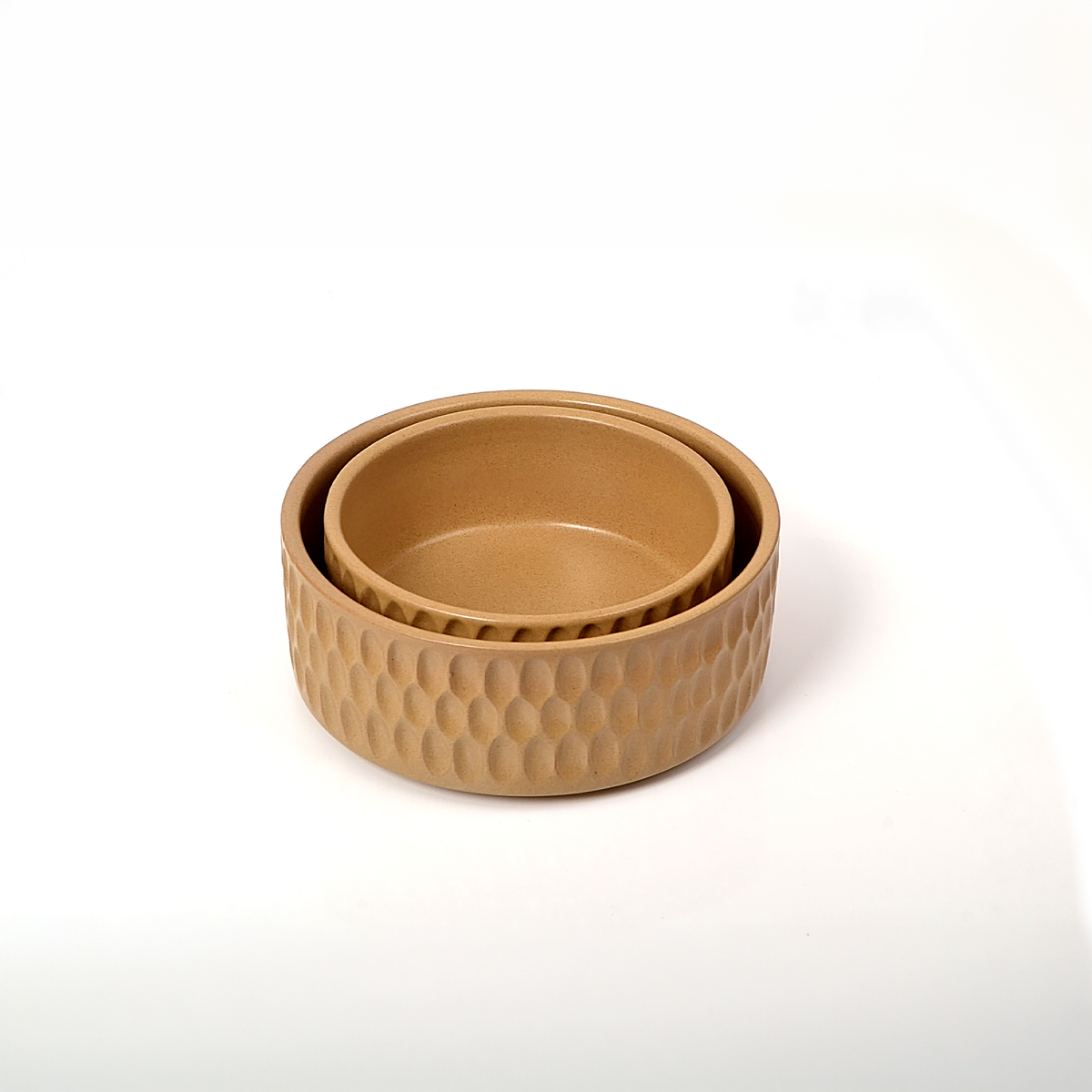 A set of three nested round bowls in a warm tan color, featuring a textured, dimpled exterior pattern and smooth interiors, photographed on a clean white background.